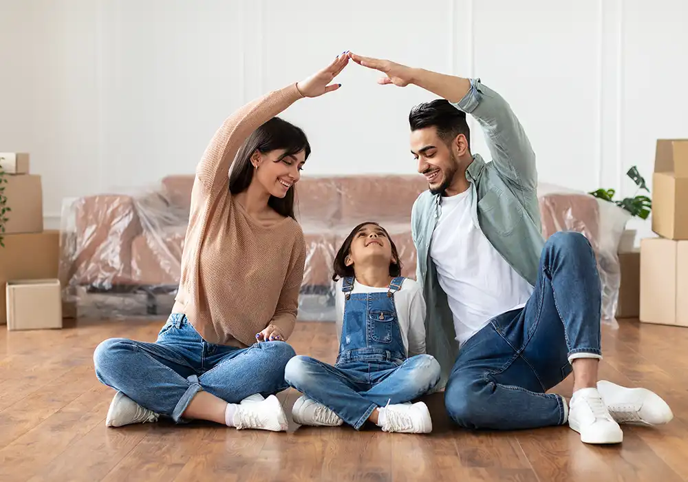 young family making a roof shape with their arms while sitting on their livingroom floor